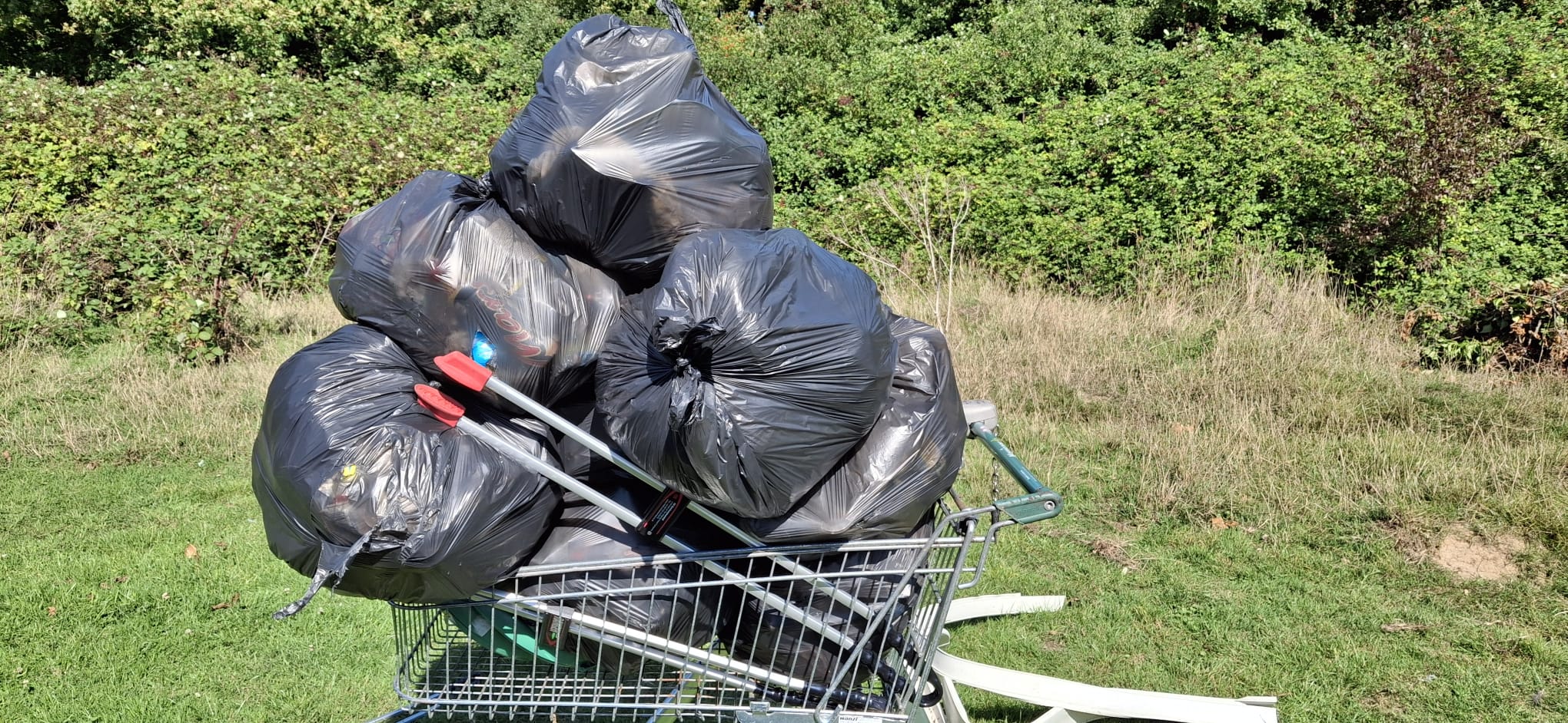An image of a discarded trolley with 10 bags of litter with a litter grabber being kept in it too