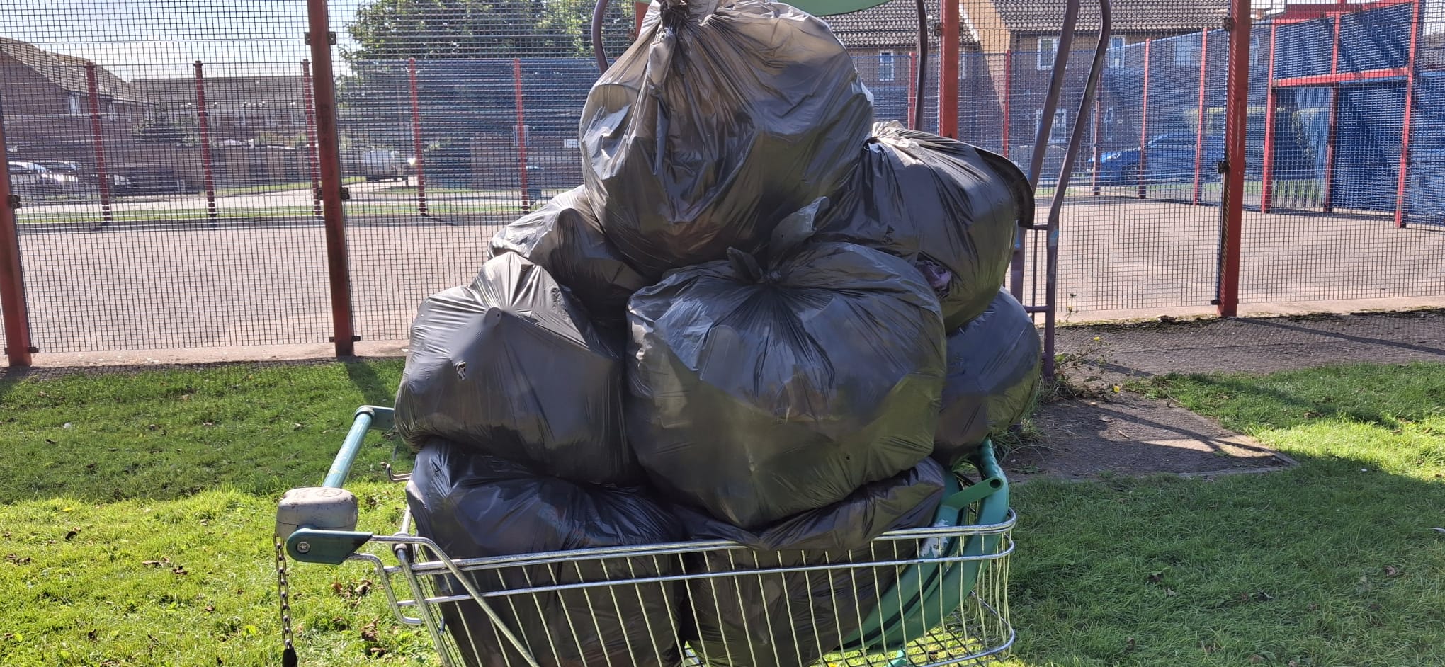An image of a discarded trolley filled with bags of litter in front of the ball park